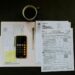 black Android smartphone near ballpoint pen, tax withholding certificate on top of white folder